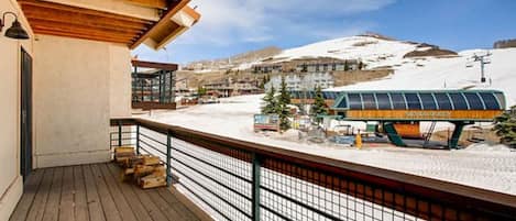A wooden deck with a metal railing overlooking a snowy landscape and a bus.