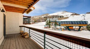 A wooden deck with a metal railing overlooking a snowy landscape and a bus. - Crested Butte Mountain Resort Properties by Vail (Crested Butte)