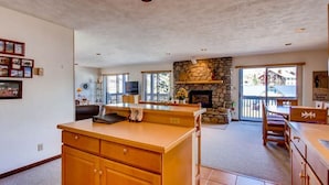 A spacious living area with a kitchen island, a stone fireplace, and large windows. - Crested Butte Mountain Resort Properties by Vail (Crested Butte)