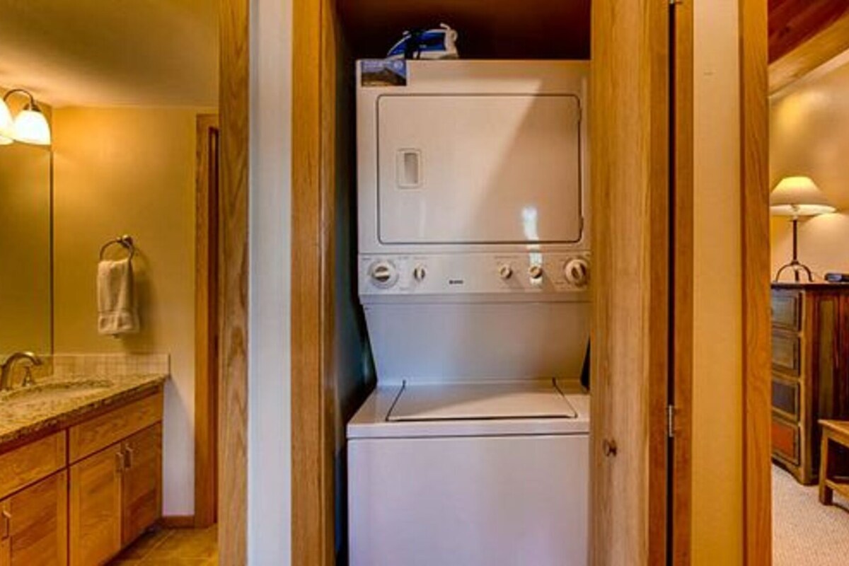 A compact laundry room with a built-in washer and dryer, wooden cabinets, and a small seating area with a chair and table.