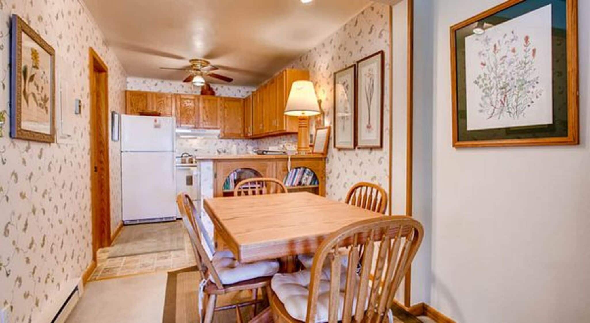 Une cuisine avec des meubles de rangement en bois, une table à manger avec des chaises et un ventilateur de plafond.
