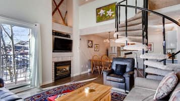 A spacious living room with a fireplace, a staircase, and a large window offering a view of the outdoors.