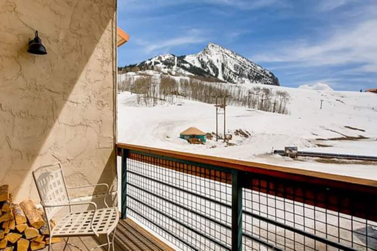 Ein Balkon mit Blick auf einen verschneiten Berg, ein Stuhl und ein Holzstapel.