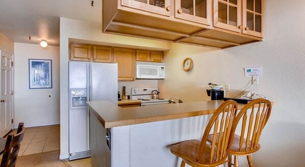 A compact kitchen with a refrigerator, microwave, and stove. There are wooden cabinets and a small island with two chairs. - Crested Butte Mountain Resort Properties by Vail (Crested Butte)