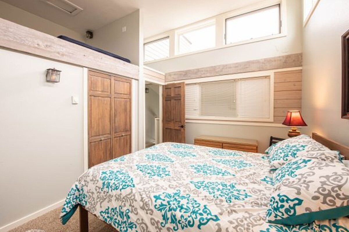 A bedroom with a bed, wooden wardrobe, and a window with blinds.