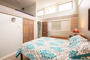 Un dormitorio con cama, armario de madera y ventana con persianas.
