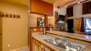 A kitchen with a double sink, wooden cabinets, a stone backsplash, and a window with curtains.