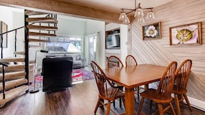 A dining area with a wooden table and chairs, a cat tree, and a television on the wall. - Crested Butte Mountain Resort Properties by Vail (Crested Butte)
