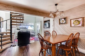 A dining area with a wooden table and chairs, a cat tree, and a television on the wall. - Crested Butte Mountain Resort Properties by Vail (Crested Butte)