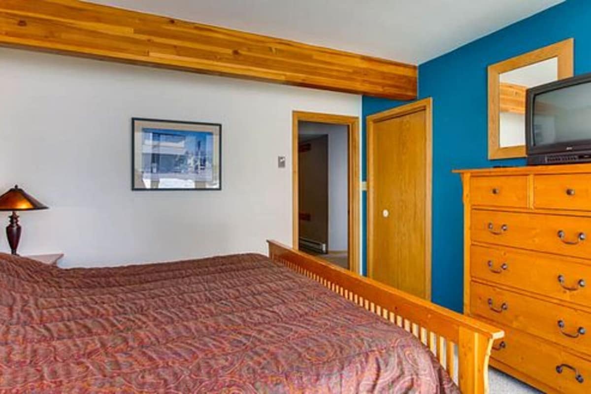 Un dormitorio con cama, cómoda, televisor y un cuadro en la pared.