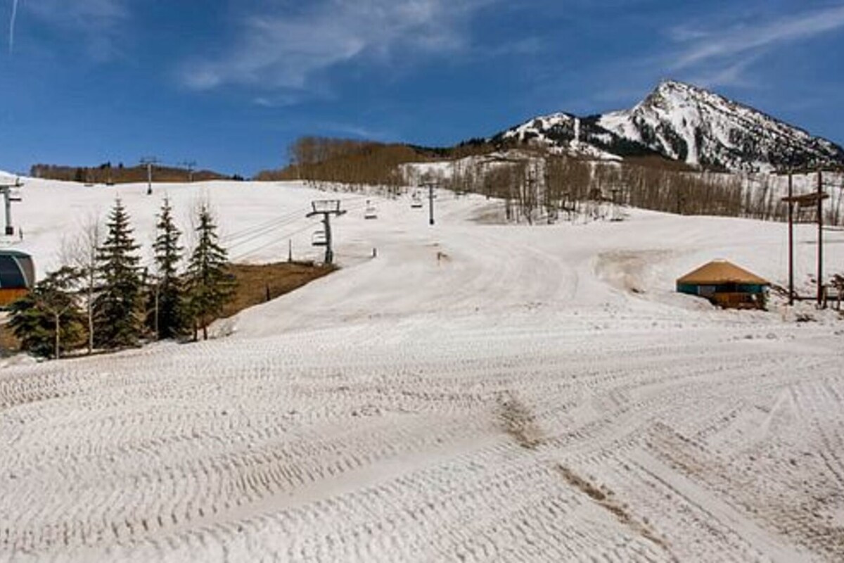 A snow-covered ski slope with ski lifts, trees, and a mountain in the background.