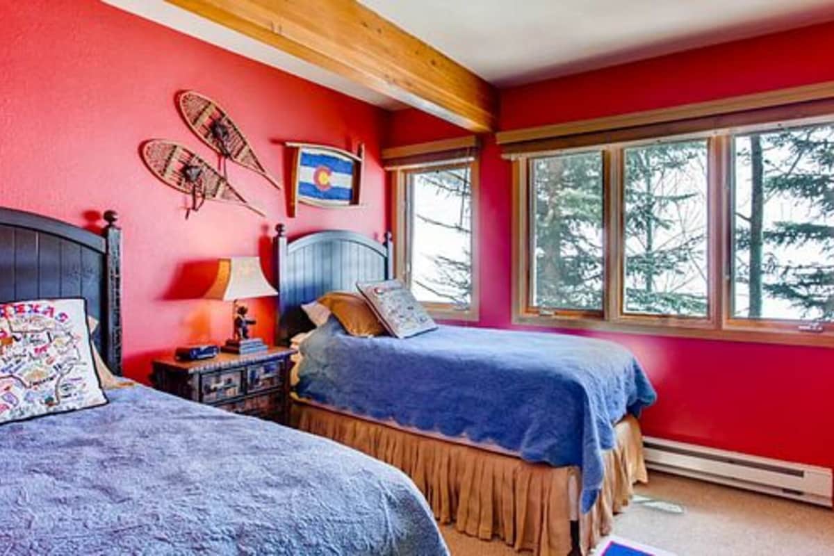 A bedroom with two beds, a wooden ceiling, a large window with a view of trees, and a flag on the wall.