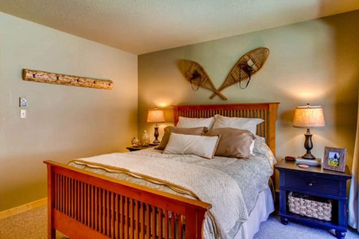 A bedroom with a wooden bed, two bedside lamps, a nightstand, and a wall-mounted decorative item.