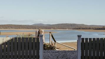 A wooden gate leading to a beach with a clear view of the water and distant hills.