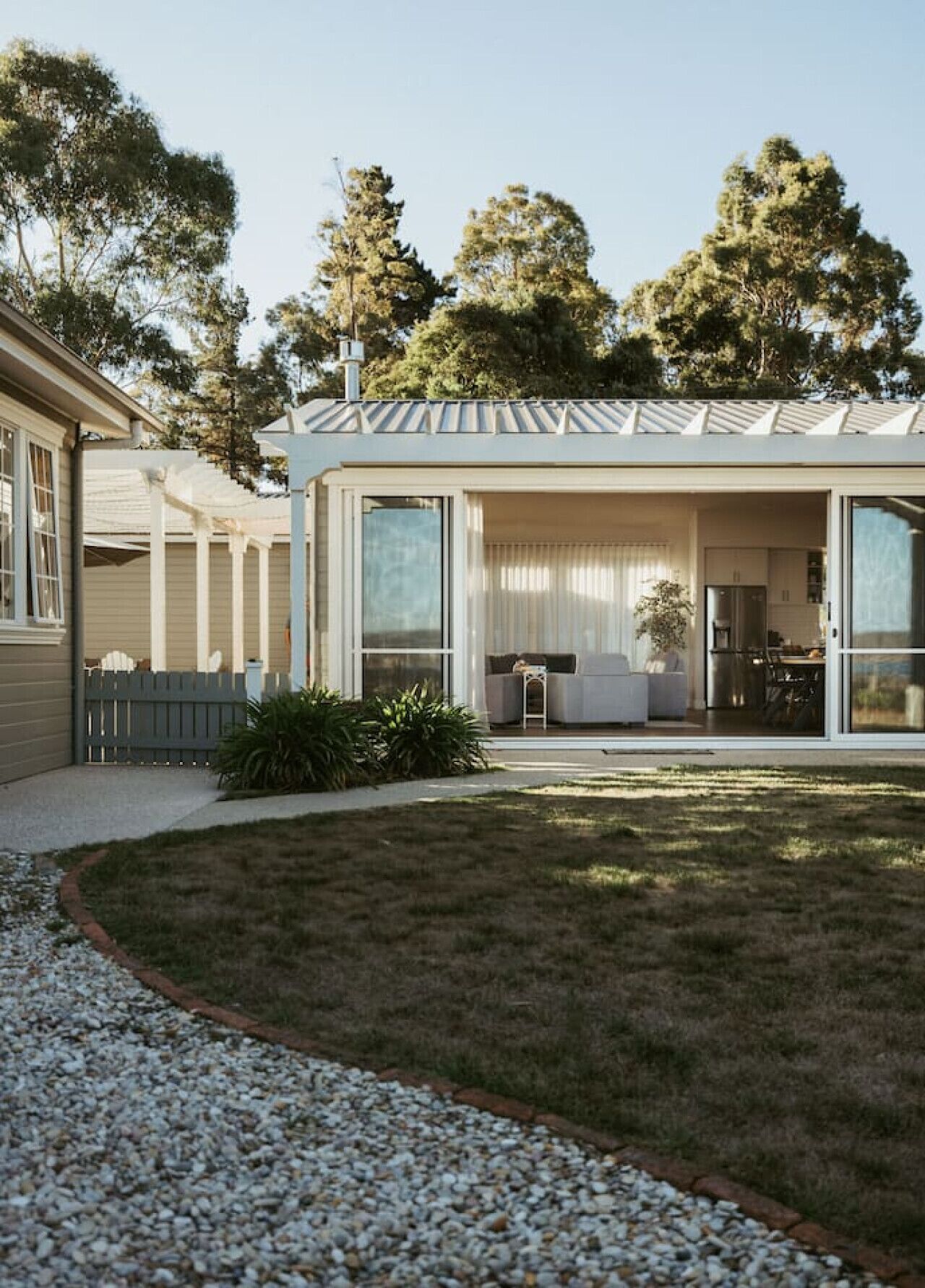 A modern house with a covered patio, a lawn, and a gravel driveway.