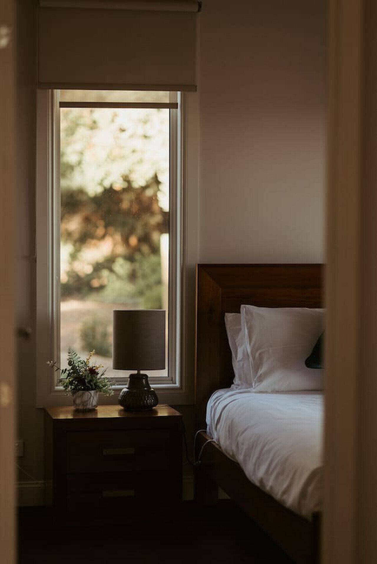 A bedroom with a bed, a nightstand, a lamp, and a window with a view of trees.