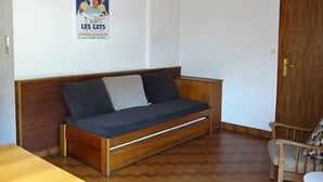 Une pièce avec un canapé en bois, une petite table et une affiche accrochée au mur.