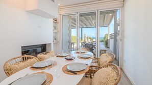 Un coin repas avec une longue table dressée pour six personnes, entourée de chaises en osier, d’un téléviseur et offrant une vue sur l’extérieur.