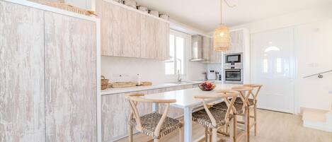 A modern kitchen with white cabinets, a central island, and a dining area with wooden chairs and a table.