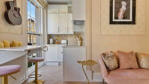 A modern kitchen with white cabinets, a bar area with stools, and a pink sofa with patterned cushions. - Apartment in Marylebone with Jacuzzi Bath (London)