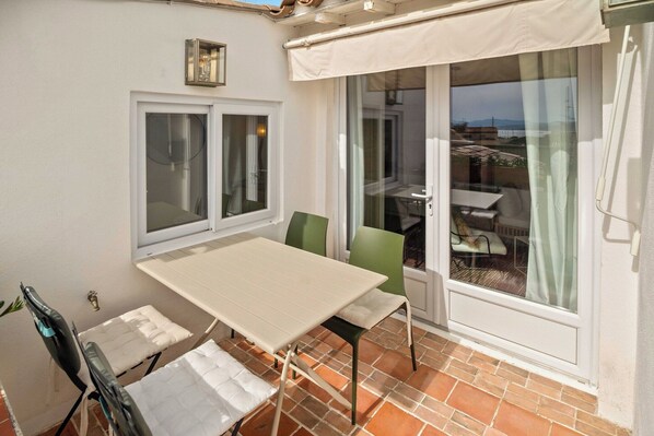 A balcony with a table and chairs, a window with curtains, and a view of the sea.