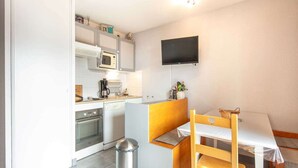 A compact kitchen with a microwave, stove, and sink, a small dining table with chairs, and a trash can.