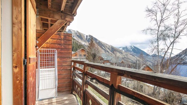 A wooden balcony with a metal railing overlooking a mountainous landscape.
