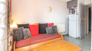 A small, cozy room with a wooden sofa, a small table, a radiator, and a refrigerator.