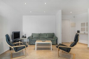 A modern living room with a green sofa, two armchairs, a coffee table, a TV, and a small side table.