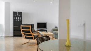 Una sala de estar moderna con una mesa de vidrio, un jarrón amarillo, un televisor y una estantería.