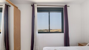 Un dormitorio con cama, un armario de madera, una ventana con cortinas y vistas al paisaje.