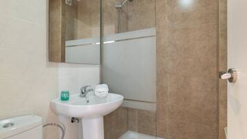 Un baño con lavamanos blanco, inodoro, ducha y espejo.