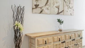 Una pared con un cuadro floral, un aparador de madera con cajones y un jarrón con una planta.