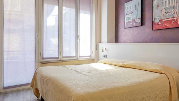 Ein Schlafzimmer mit einem Bett, einem Fenster und zwei an der Wand befestigten Bildern.
