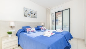 A modern bedroom with two beds, a nightstand, a potted plant, and a painting on the wall.