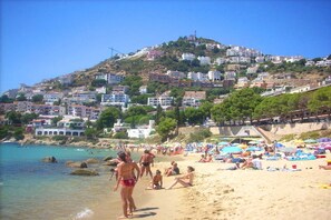 Une plage où des gens se prélassent au soleil et se baignent, entourée de bâtiments situés sur une colline.