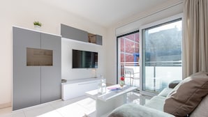 A modern living room with a flat-screen TV mounted on the wall, a white coffee table, and a grey sofa.