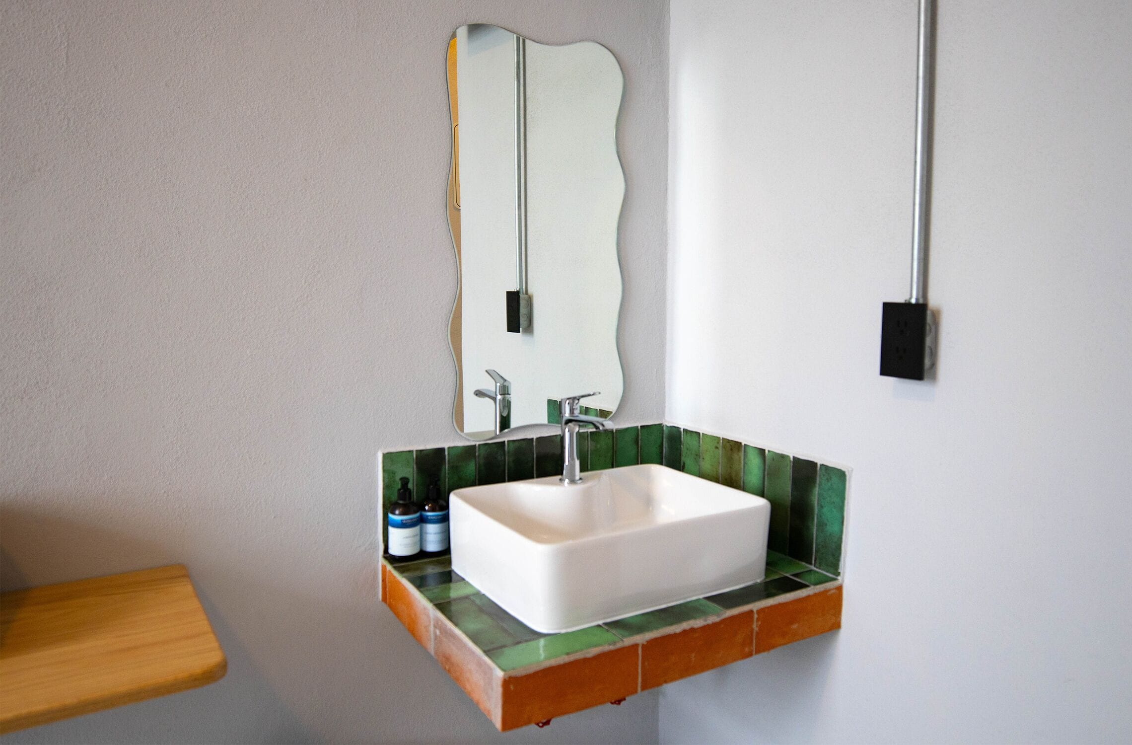 A bathroom with a white sink, green and orange tiled countertop, and a mirror above it.