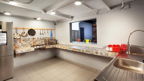 Een kleine keuken met een magnetron, fornuis en spoelbak. Er hangen pannen en er is een raam met uitzicht.