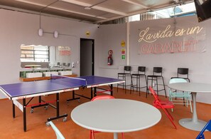 A ping pong table, chairs, and a neon sign in a room with a tiled floor. - Hostal Casa MX Bellas Artes (Mexico City)