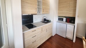 Eine kompakte Küche mit Holzausstattung, einem schwarzen Induktionskochfeld, einer Mikrowelle und einer Kaffeemaschine.
