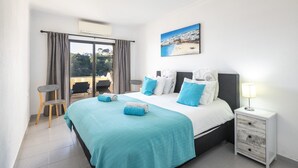 A bedroom with a bed, a nightstand, a chair, a window with curtains, and a painting on the wall. - Casa Colina Sol 611 - Seaview apartment (Carvoeiro)