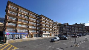 Un edificio residenziale a più piani con balconi, un ingresso a livello strada e un parcheggio con auto.