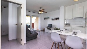 Una cucina moderna con mobili bianchi, un'area pranzo con tavolo e sedie bianche, un divano grigio e una ventola a soffitto.
