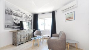 Ein Wohnzimmer mit Fernseher, Schrank, einem Gemälde und einem Fenster mit Vorhängen.