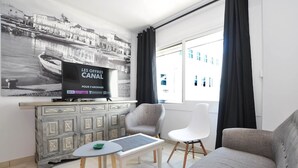 Ein modernes Wohnzimmer mit einem grauen Sofa, einem weißen Sessel, einem kleinen Tisch und einem Fernseher auf einer Kommode.