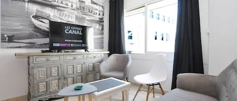 Ett modernt vardagsrum med en grå soffa, en vit fåtölj, ett litet bord och en tv som står på ett skåp.
