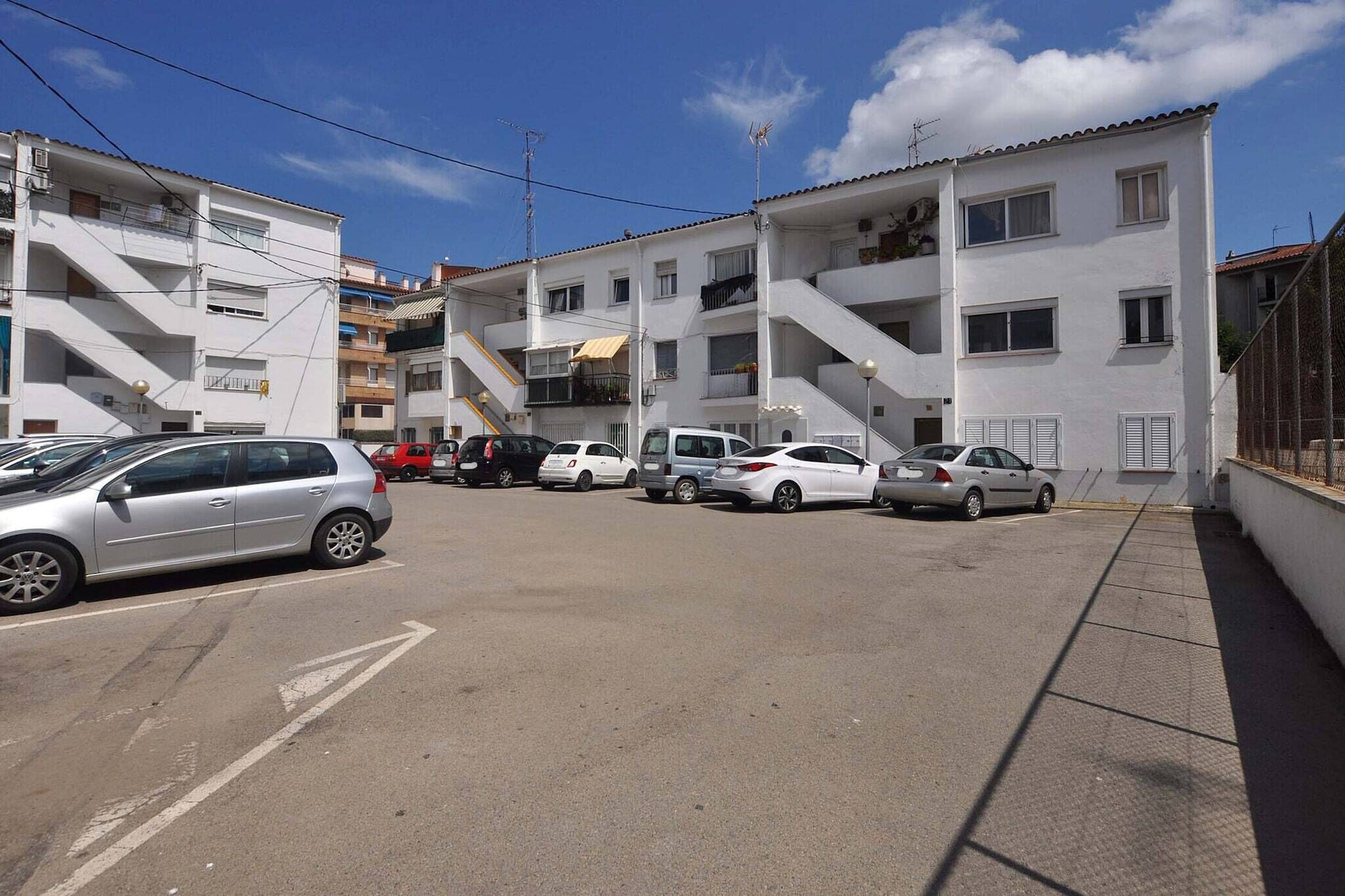 A parking lot with several cars parked in front of a white building with multiple balconies and windows.