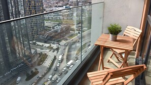 Ein Balkon mit Glastrennwand, Holzstühlen, einem kleinen Tisch und einem Blumentopf.