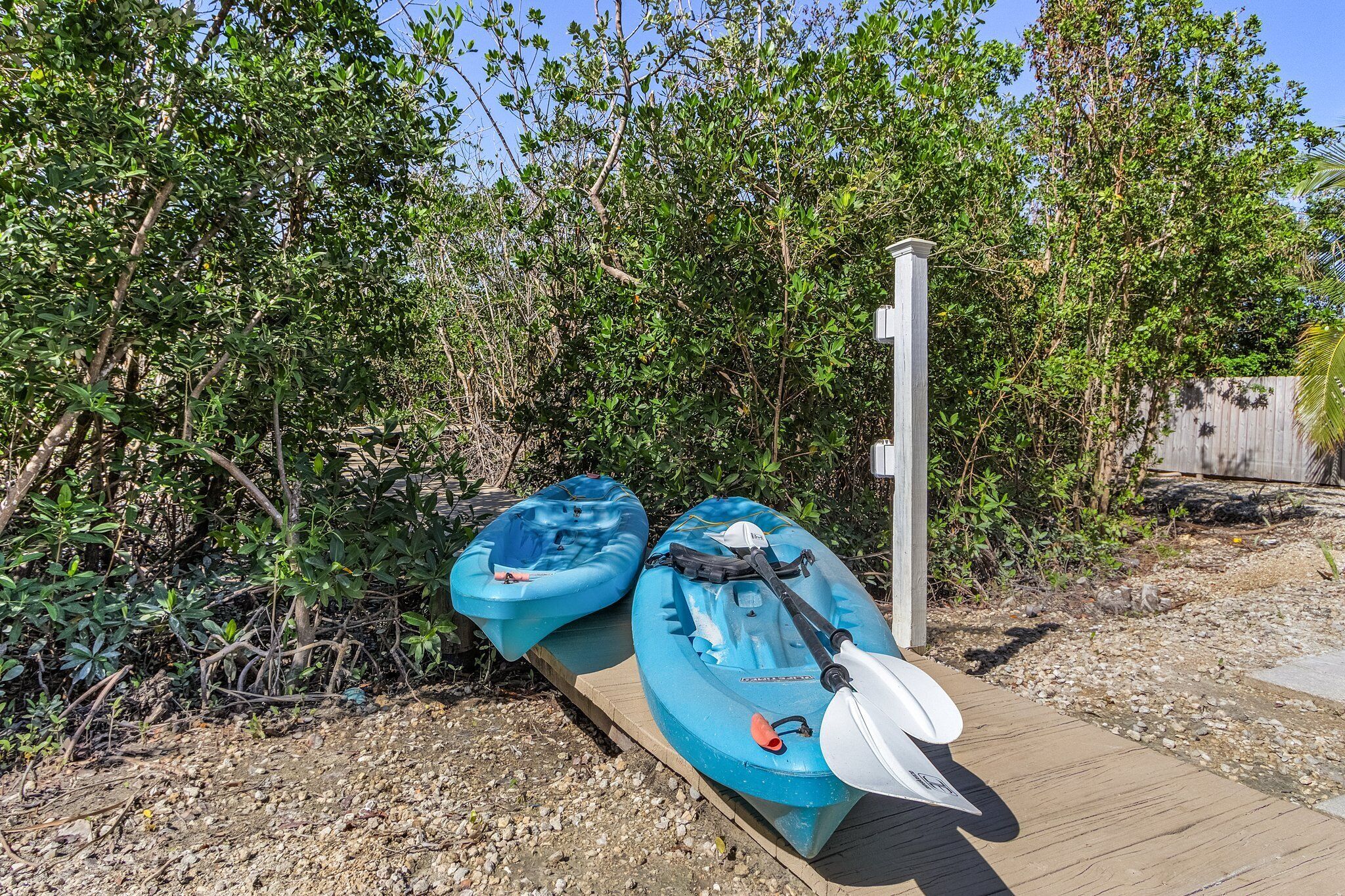 Two kayaks on a wooden dock with a wooden fence and dense foliage in the background.